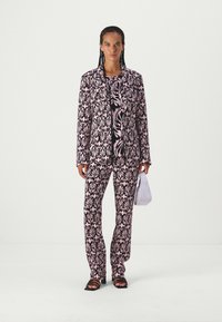 Floral-patterned suit in black and pink with a tailored jacket and matching pants. Accessorized with a white bag and black sandals.