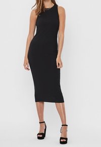 Robe midi noire côtelée sans manches avec un col rond. Associée à des talons compensés noirs avec des brides à la cheville.