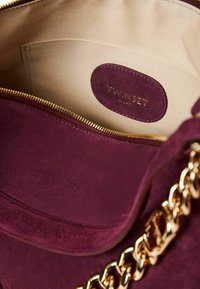 Borsa in suede bordeaux con zip dorata, con fodera beige e etichetta impressa con "TWINSET" in oro. Visibile tracolla a catena.