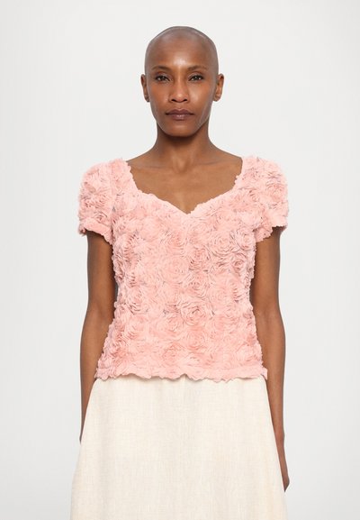 Blusa texturizada rosa con flores, de manga corta y escote amplio, con un diseño en capas que recuerda a los pétalos de rosa. Tejido suave.
