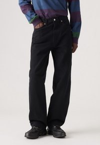 Svarta denimjeans med raka ben, fem fickor och kopparfärgad hårdvara, i kombination med texturerade svarta sneakers.