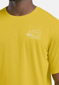 T-shirt gialla realizzata in tessuto leggero con design a tratto bianco e logo sul petto. Maniche corte, scollatura a girocollo.