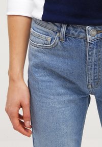 Ljusblå denimjeans med slim fit, femfickdesign och metallknappslås. Tyget visar lätt blekning och textur.