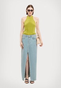 Zelený bezramínkový halter top, modrá džínová maxi sukně s předním rozparkem, černé sandály na blokovém podpatku a malá béžová crossbody taška.