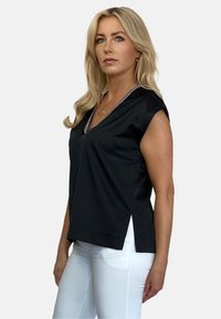 Czarny bezrękawnik z dekoltem w serek, ozdobiony białym wykończeniem. Posiada prosty fason i boczne rozcięcia dla swobody ruchów. Gładki materiał.