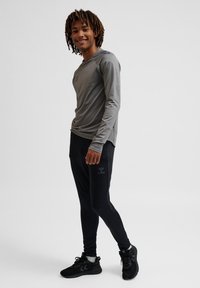 Camisa deportiva de manga larga gris claro combinada con joggers negros ajustados. Los joggers cuentan con un logo sutil, y la textura parece suave y elástica.