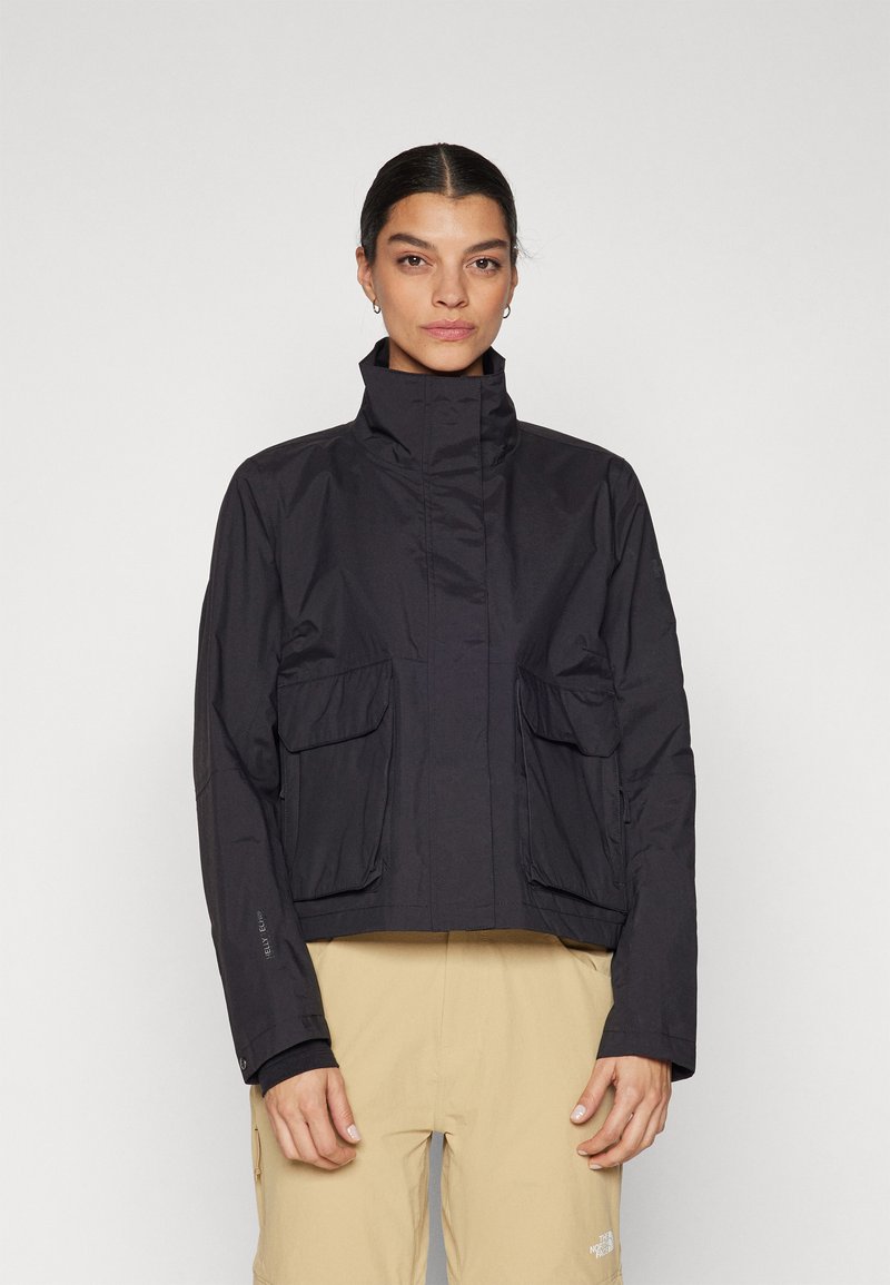 Chaqueta negra impermeable con un alto cuello, dos bolsillos frontales y un diseño corto. Textura suave con un discreto logotipo en la manga.