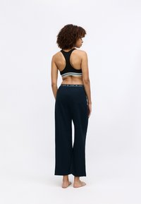 Zwarte sportbeha met racerback ontwerp, voorzien van een gestreepte band. Marineblauwe wijde broek met een elastische tailleband en logo-detail.