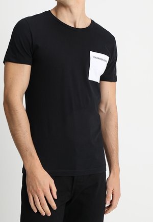 T-shirt in cotone nero con colletto tondo e taschino bianco sul petto con il logo "CALVIN KLEIN JEANS". Tessuto morbido, vestibilità standard.