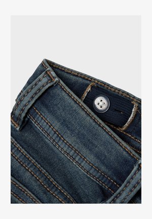 Dunkelblaue Jeans aus Denim mit sichtbaren Nähten, einem Knopfverschluss und Gürtelschlaufen, mit glatter Textur und leichter Verblassung.