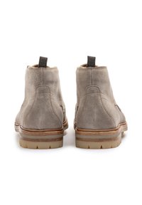 Botas de tobillo de ante gris con suela marrón claro, que presentan un tacón texturizado y una tira de sujeción. El diseño incluye acentos cosidos y un patrón de banda de rodadura resistente.