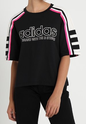 Black cotton t-shirt with oversized fit, featuring pink and white stripes on sleeves and "adidas" logo text centered on the front.