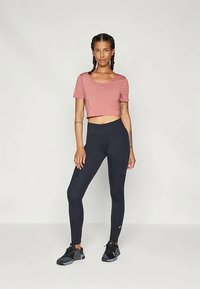 Rozā sporta tops ar īsu piegriezumu un melnā augstā jostasvieta legingi, ar gludu tekstūru un logo akcentiem, papildināti ar melniem sporta apaviem.