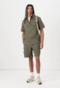 Oliven grøn kortærmet skjorte og cargo shorts, lavet af et letvægtsmateriale. Har lappelommer, knapper og en afslappet pasform.