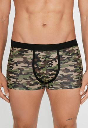 Männlicher Oberkörper, bekleidet mit grün-braun-schwarzen Camouflage-Boxershorts mit schwarzem Bund und Besatz.