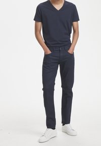 Camiseta de cuello en V de color navy combinada con jeans oscuros y zapatillas blancas. Material de algodón, diseño ajustado, con bolsillos frontales y cintura clásica.