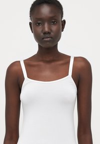 Witte camisole met dunne bandjes, met een aansluitende ontwerp en een soepele textuur. Eenvoudige en minimalistische stijl zonder patronen of versieringen.