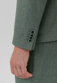 Veste de costume verte texturée avec quatre boutons noirs sur les poignets, mettant en valeur un design ajusté et une finition en tissu lisse.