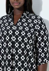 Czarna i biała bluzka w wzory z motywem kwiatowym, z ostrym kołnierzykiem i rękawami do łokcia o gładkiej fakturze.