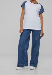 Hvid bomulds T-shirt med blå raglan ærmer, kombineret med brede blå denim cargo bukser med sidelommer og syninger.