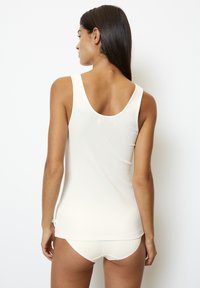 Top in maglia a coste color crema con scollatura a rovescio; abbinato a slip in maglia a coste color crema. Tessuto morbido e leggero con un design aderente.