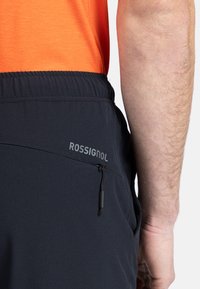 Schwarze Shorts mit einem elastischen Bund und einer Reißverschlusstasche. Mit einem in grau auf der Seite aufgedruckten Logo "ROSSIGNOL". Glatte Stofftextur.
