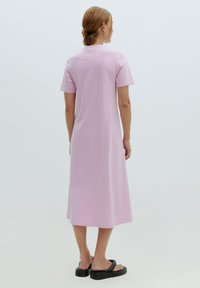 Rosa, kurzärmliges, knielanges Kleid aus weichem Stoff mit lockerer Passform. Getragen mit schwarzen Plateausandalen. Minimalistisches Design, keine sichtbaren Muster.