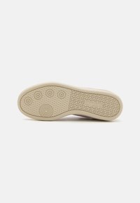 Shoe outsole featuring a light beige rubber material, circular and patterned grooves for grip, with a distinctive logo and branding detail.