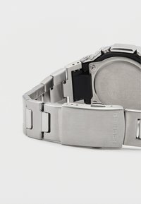 Hõbedane roostevabast terasest G-Shock kellarihm, millel on harjatud viimistlus, klapitav kinnitus ja ruudukujuline linkide disain.