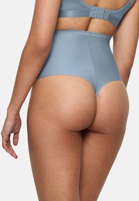 Kvinna som bär högmidjade ljusblå stringtrosor och matchande bh med hak- och ögllås, sedd bakifrån.