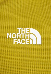 Tela amarilla texturada con un gran logotipo blanco de "THE NORTH FACE" que presenta un diseño en media luna.