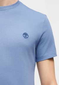 Ανοιχτό μπλε κοντομάνικο μπλουζάκι με μικρό σκούρο μπλε λογότυπο δέντρου κεντημένο στο αριστερό στήθος.