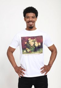 Hvid bomulds t-shirt med et farverigt print af et blomsterstilleben med pæoner mod en rød baggrund og tekst nederst.