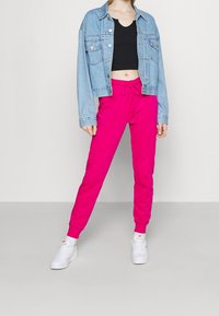 Giubbotto in denim di colore azzurro chiaro, top corto nero e pantaloni jogger rosa acceso con coulisse. Le sneakers bianche completano l'outfit.