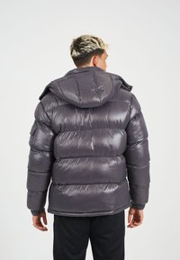 Gevoerde hooded jas in donkergrijs, glanzend materiaal. Voorzien van gestikte secties, elastische manchetten en een ritssluiting aan de voorkant.