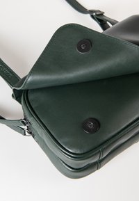 Borsa in pelle verde con un design strutturato, dotata di chiusura a pattina e bottoni a pressione neri. Texture liscia con bordi arrotondati.