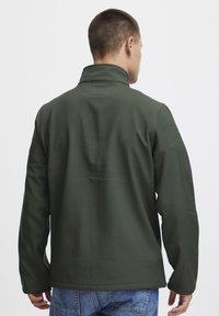 Dark green jacket with a high collar and long sleeves. Smooth, texture with a relaxed fit. Notable stitching along the seams.
