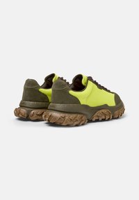 Zapatillas verdes y amarillas neón con una suela marrón gruesa, que muestran un diseño deportivo y una tela texturizada en la parte superior.
