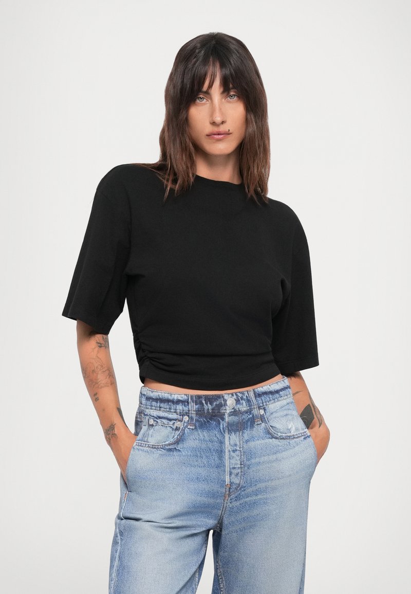 Schwarzes Cropped-Top mit kurzen Ärmeln und rundem Ausschnitt, kombiniert mit hochgeschnittenen hellblauen Jeans aus Denim. Glatte Textur und lockere Passform.