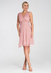 Ärmeloses pinkes Kleid mit einem gewickelten Oberteil und gerafftem Taillenbereich. Der fließende Rock hat ein dezentes Texturmuster und endet oberhalb des Knies.