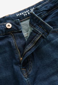 Jeans din denim închis, cu croială dreaptă, cu închidere cu fermoar și buton. Prezintă accesorii din cupru și detalii de cusătură contrastante portocalii.