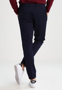 Granatowe spodnie o zwężanym kroju, wykonane z lekkiego materiału, z dwoma tylnymi kieszeniami, noszone z białymi trampkami.