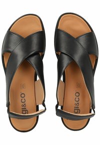 I sandali neri in pelle presentano un design a strap incrociati, punta aperta e una soletta imbottita color tan con branding. Texture liscia, hardware minimal.