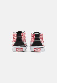 Baskets montantes Vans noires et rouges avec un motif de logo répétitif, semelles blanches et accents en suède noir. Finition en tissu texturé.
