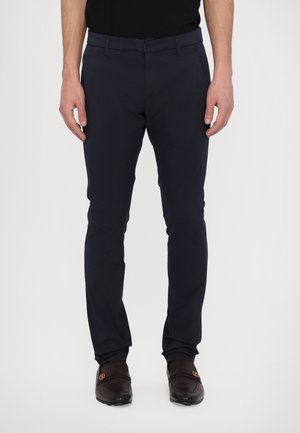 Navy chinos with a slim fit design, made of cotton, featuring a belt loop, zipper fly, and side pockets. Smooth texture, minimalistic style.