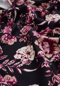 Tissu noir avec un motif floral détaillé comprenant de grandes fleurs crème, roses et bordeaux ainsi que des feuilles, présenté avec des plis doux et une texture apparente.