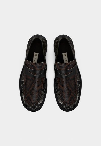 Ζευγάρι μοκασίνια με μοτίβο από δέρμα φιδιού σε μαύρο και καφέ χρώμα, με μαύρο λουρί από πάνω, απεικονισμένα από πάνω σε λευκό φόντο.