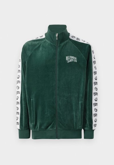 Jacket verde de veludo com fecho, gola alta, bolsos laterais e mangas brancas com um padrão que apresenta o logo e detalhes da "Billionaire Boys Club".