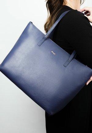 Sac fourre-tout en cuir navy avec deux poignées, texture lisse et un subtil accent logo doré à l'avant.