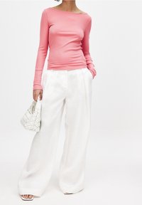 Långärmad, ribbad rosa topp i kombination med lösa, vita linnebyxor. Outfiten kompletteras av en liten, vävd vit handväska.